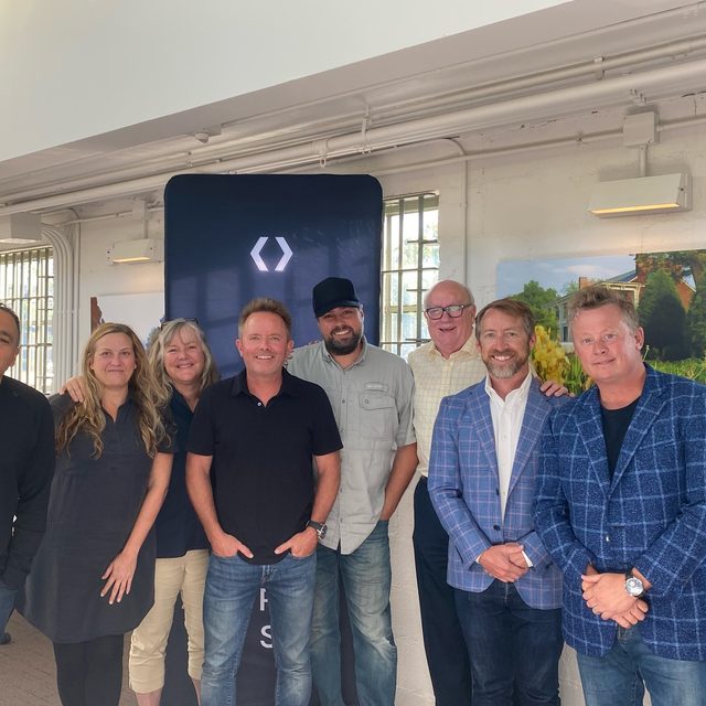 Erik Dellenback with Chris Tomlin and the For Others board, standing in a line in a bright loft
